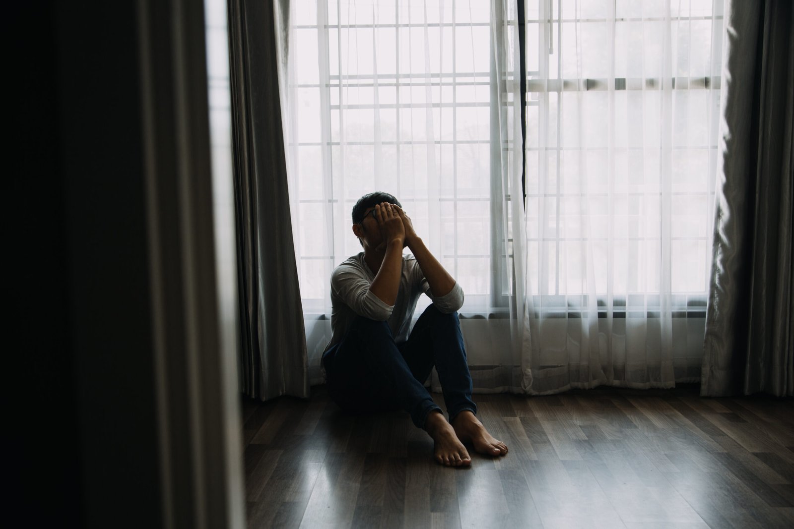 Alone man silhouette staring at the window closed with curtains in bedroom. Man stands at window alone